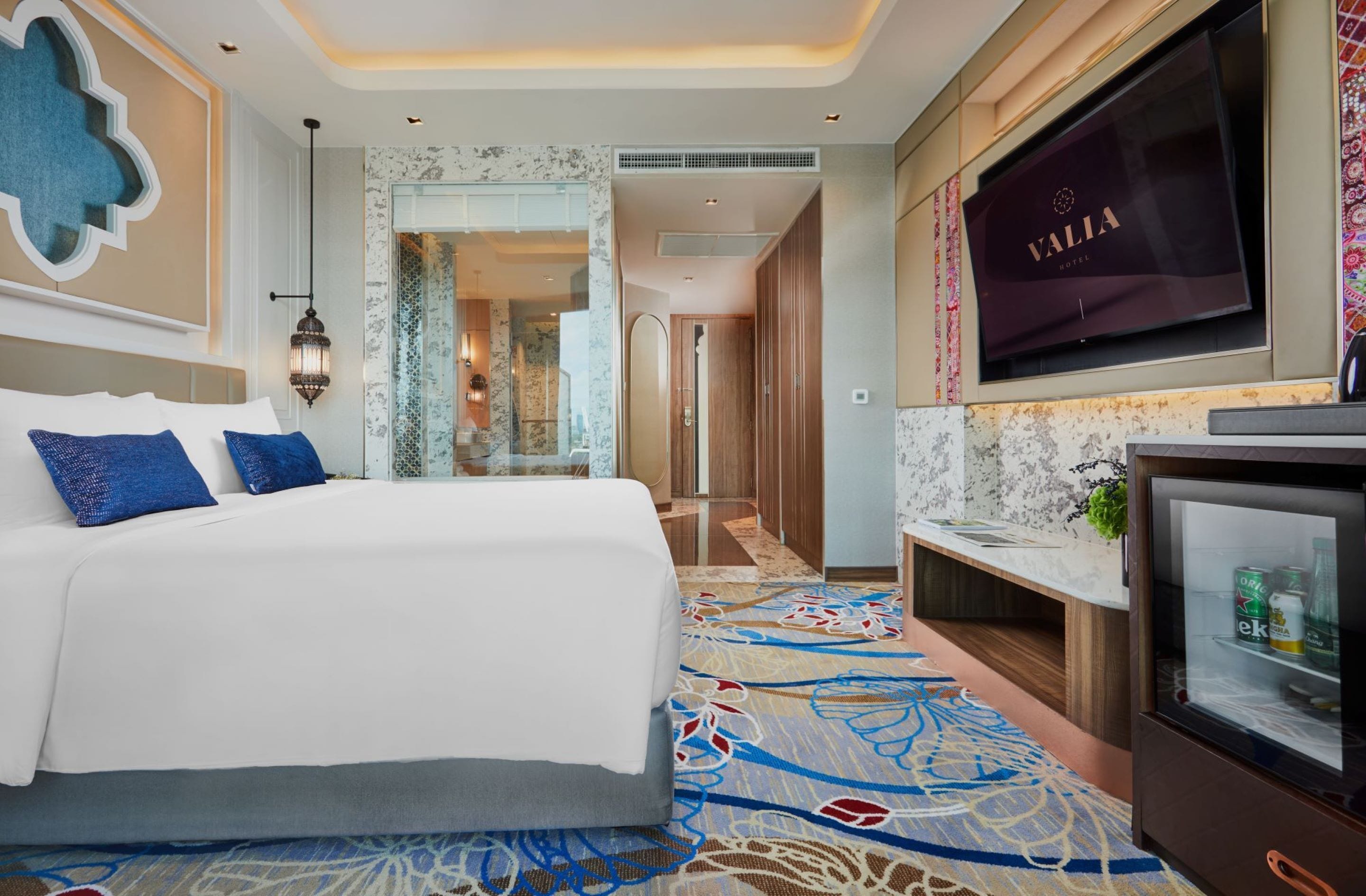 Une chambre d’hôtel avec un grand lit, une télévision, un minibar et une moquette à motifs.