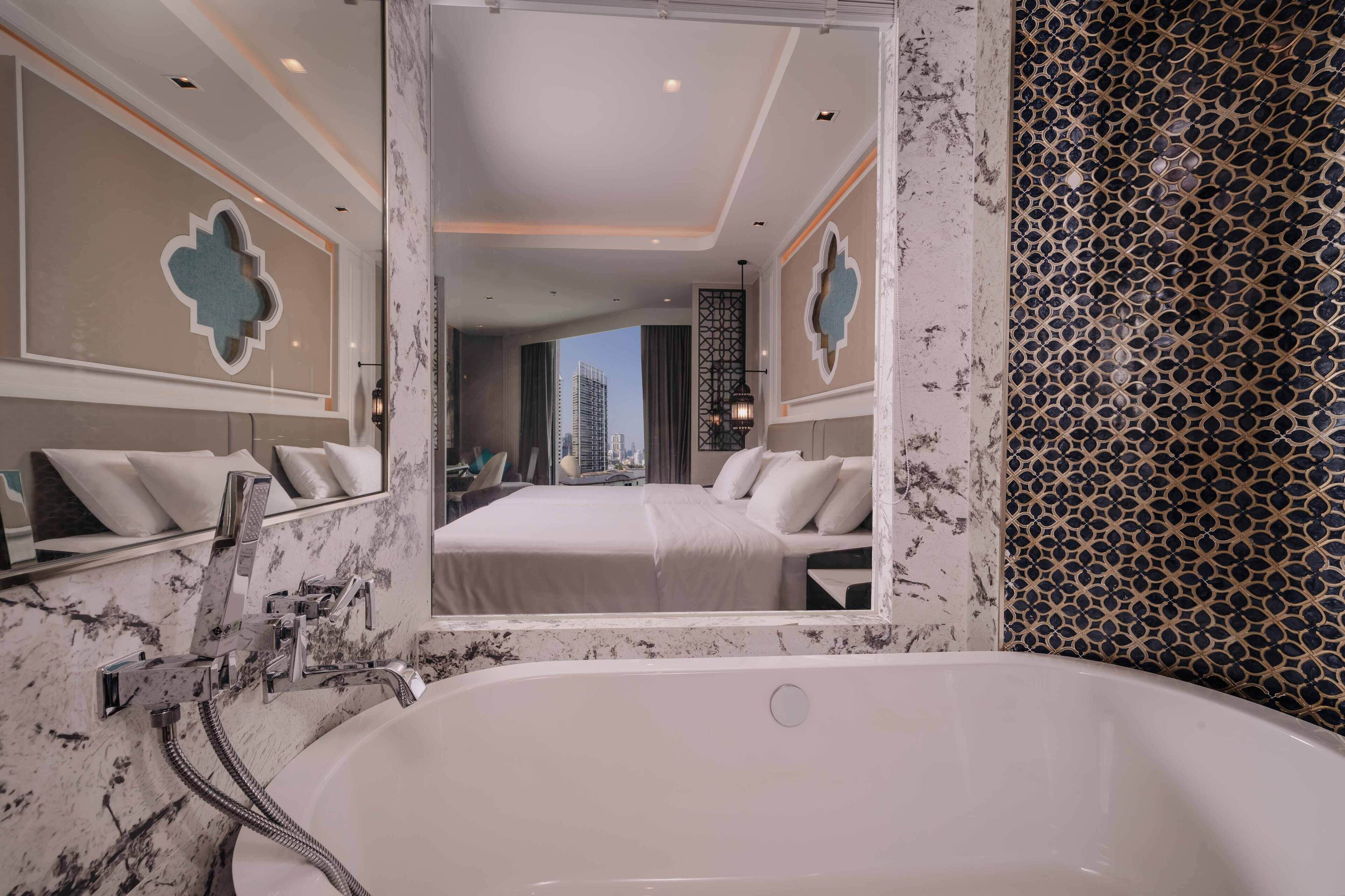 A modern bathroom with a large mirror, a bathtub, and a bed with a city view.