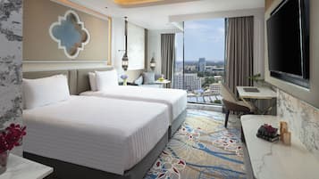 A hotel room with two beds, a desk, a TV, and a view of the city.