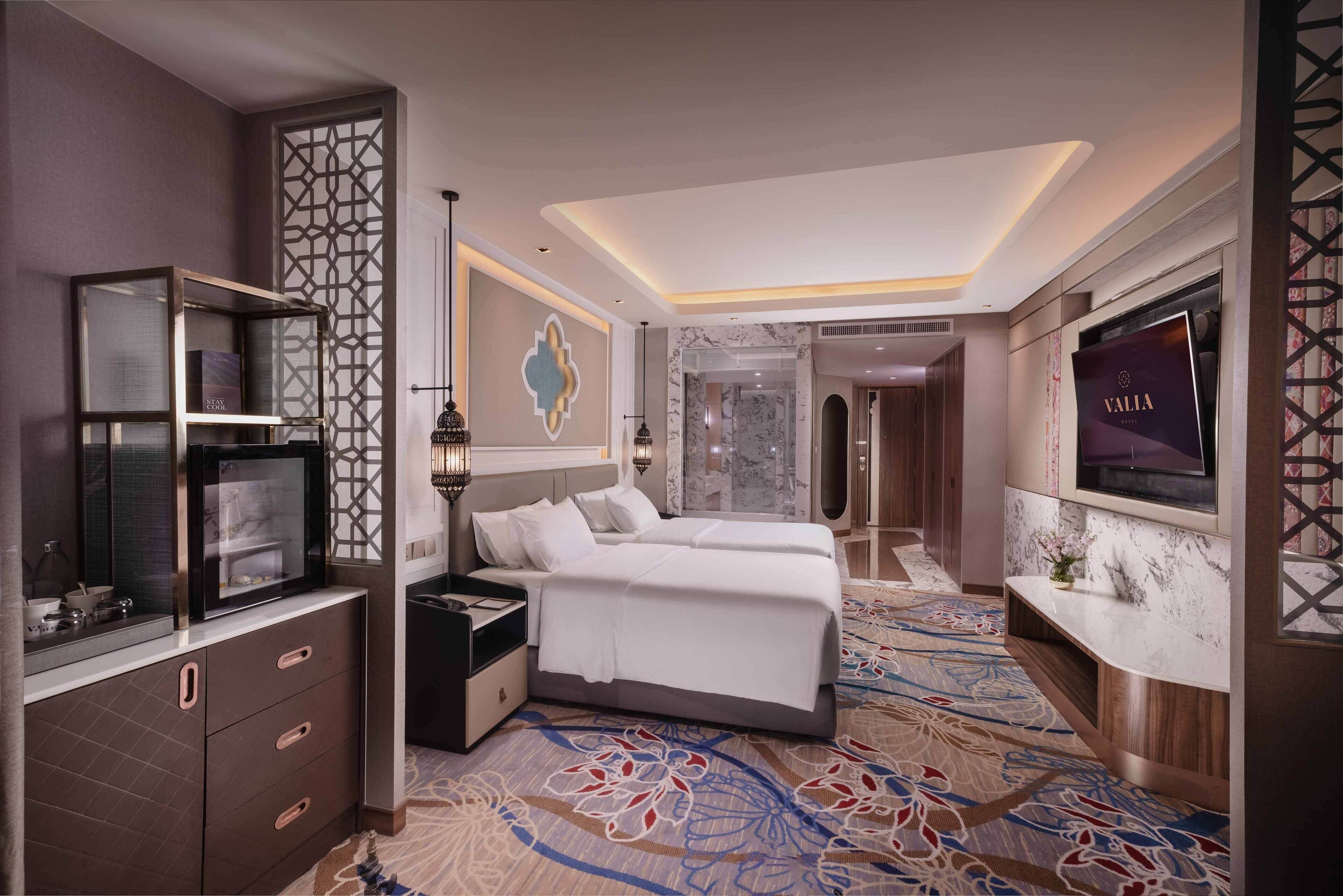 A hotel room with a large bed, a TV, a minibar, and a decorative wall panel.