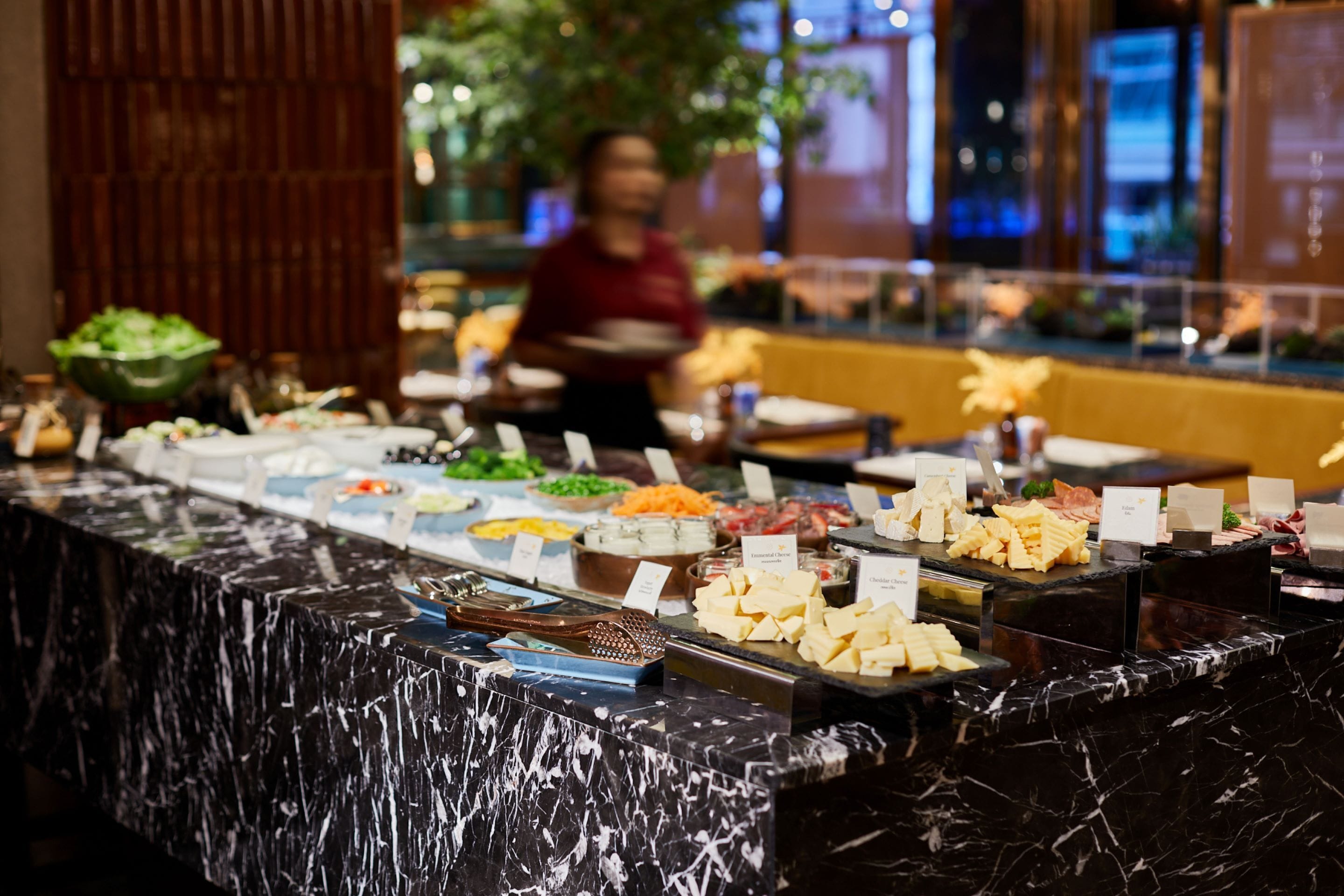 A buffet with various food items and a server in the background.