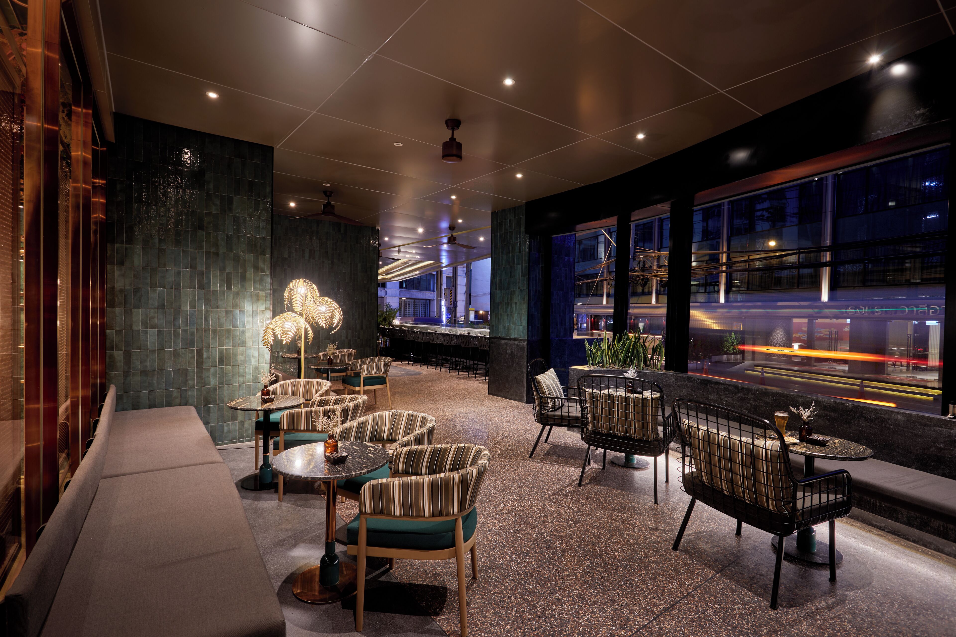 A modern lounge area with seating arrangements, a bar, and large windows offering a view of the cityscape.