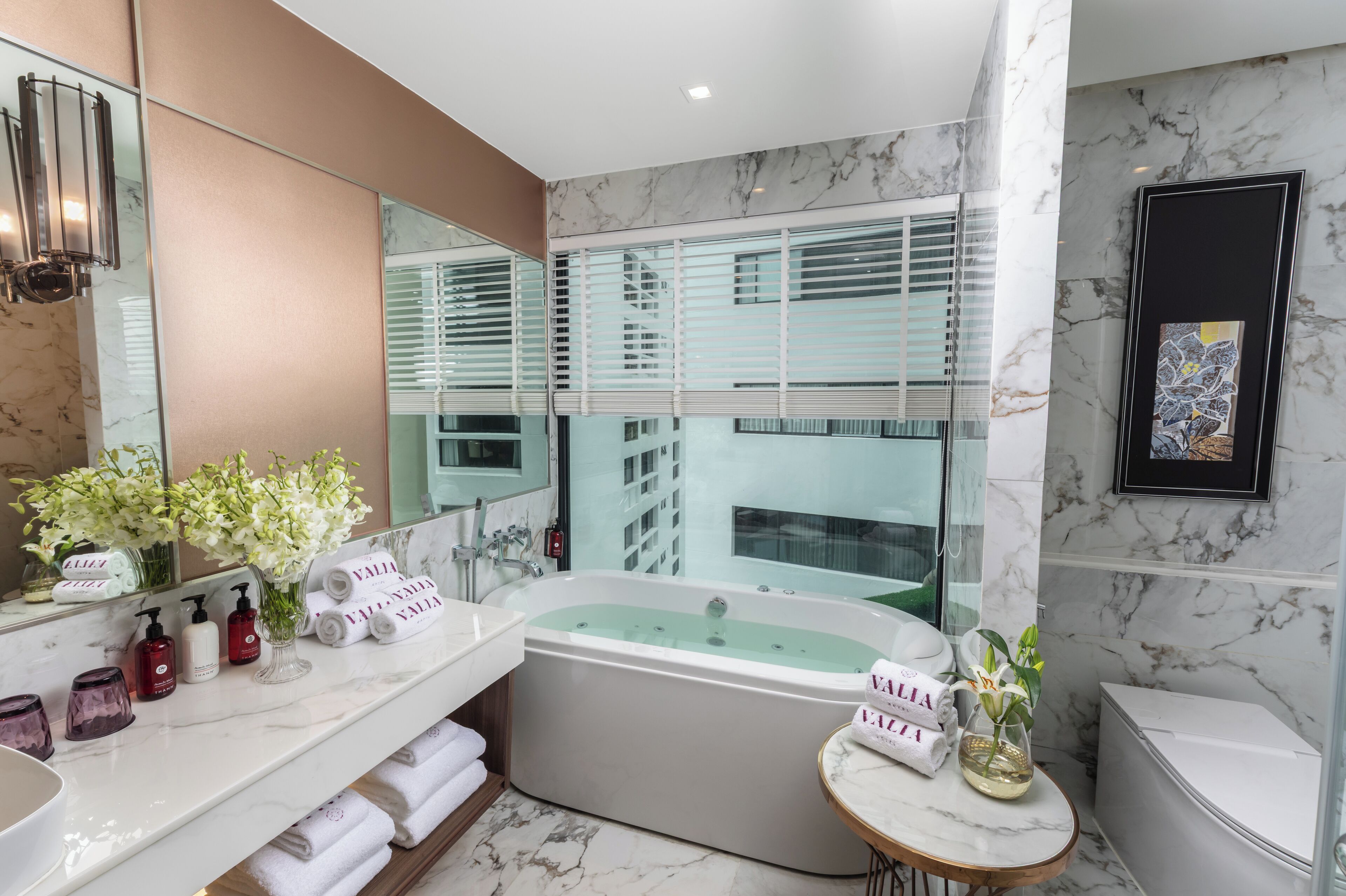 A modern bathroom with a large bathtub, two sinks, a vanity, and a window with blinds.