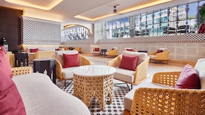 A modern lounge area with wicker furniture, a patterned wall, and a large window offering a view of the city. - Valia Bangkok Sukhumvit 24 by Kingston Hotels (Bangkok)