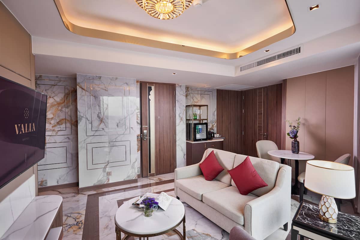 Rebedor modern d'hotel amb sòl de marbre, un sofà amb coixinets vermells, un televisor i una taula petita amb un ram de flors.