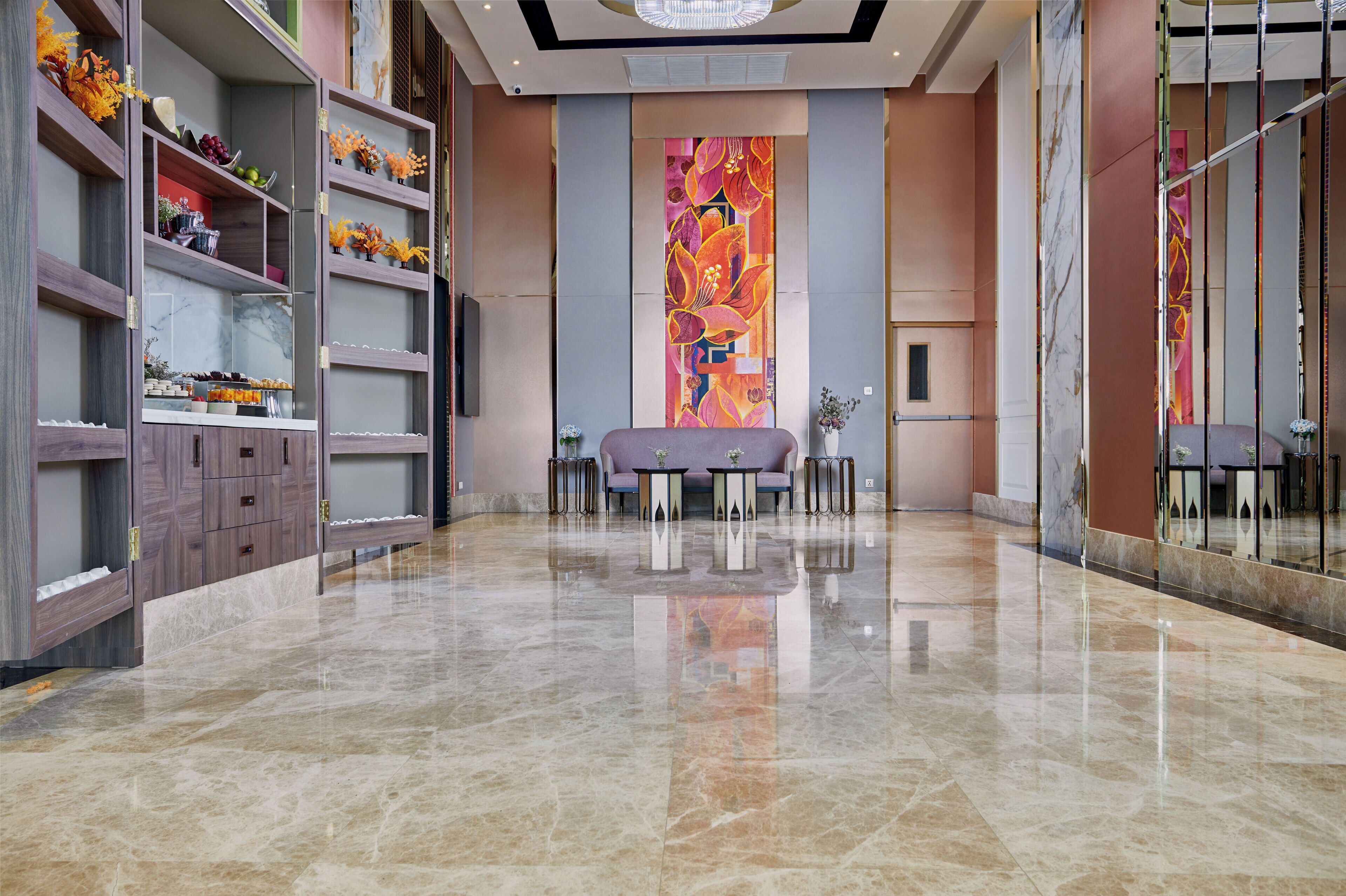 A spacious lobby with a marble floor, a large floral mural, and a seating area with tables and chairs.