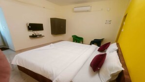 A hotel room with a bed, a TV, a wardrobe, and a green chair. - PPH Living Royal Pride (Madurai)