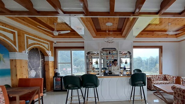 A spacious room with a bar area, seating, and large windows offering a view of the outdoors. - ABHILASHI INN (Balh)