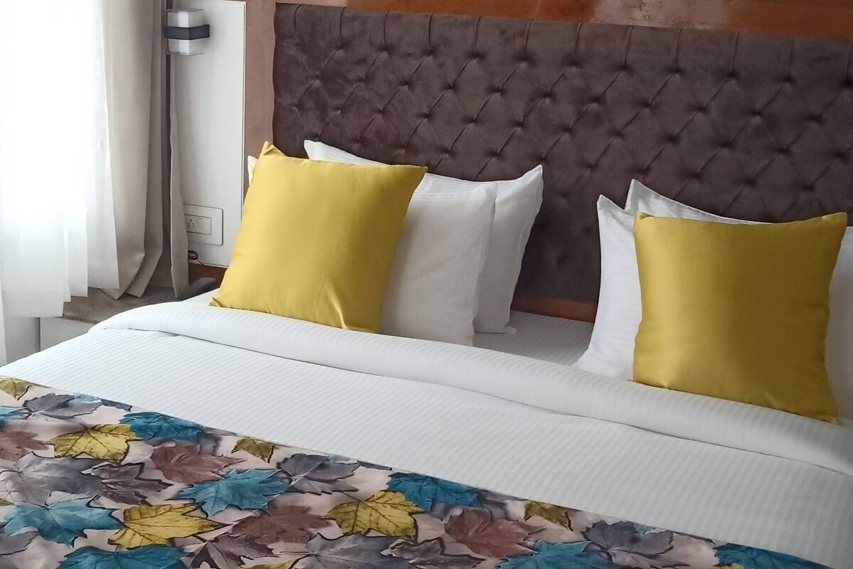 Habitación de hotel con cama, cabecera, aire acondicionado instalado en la pared y ventana con cortinas.