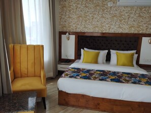 A hotel room with a bed, a wooden nightstand, a yellow armchair, and a patterned wall. - ABHILASHI INN (Balh)