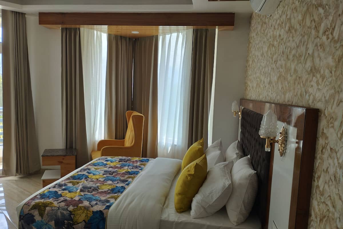 Una habitación de hotel con cama, una silla, una mesita de noche y un ventanal con cortinas.