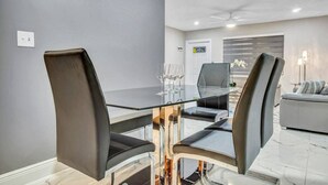 A modern dining area with a glass table and black chairs, a grey sofa, and a ceiling fan.