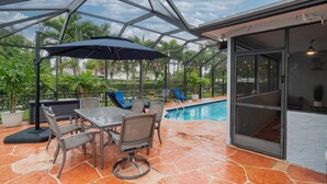 An outdoor patio with a pool, covered seating area, and a table with chairs.