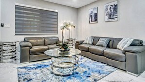 A modern living room with a sectional sofa, a glass coffee table, and a large window with blinds.