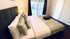 Ein Schlafzimmer mit Bett, Nachttisch, Fenster mit Vorhängen und Kleiderschrank.
