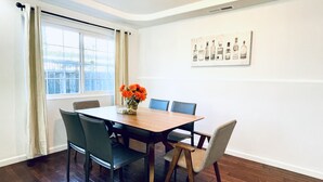 Ein Esszimmer mit einem Holztisch, vier Stühlen und einer Vase mit orangefarbenen Blumen.