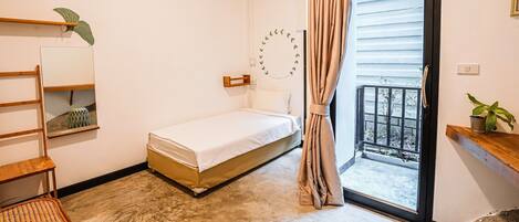 A bedroom with a bed, a wooden chair, a small table, a mirror, and a balcony with a curtain.