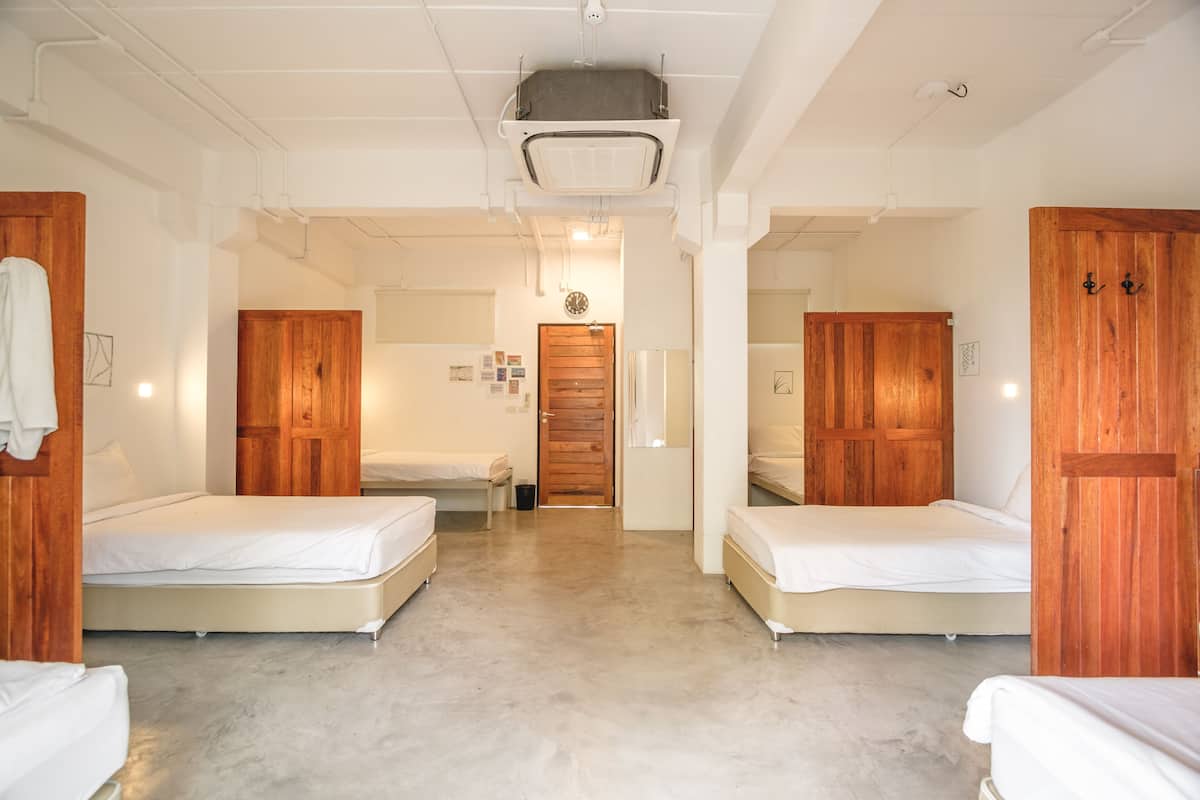 Ein Hotelzimmer mit zwei Betten, Holzschränken, einer kleinen Küchenzeile und einem Badezimmer mit Holztür.