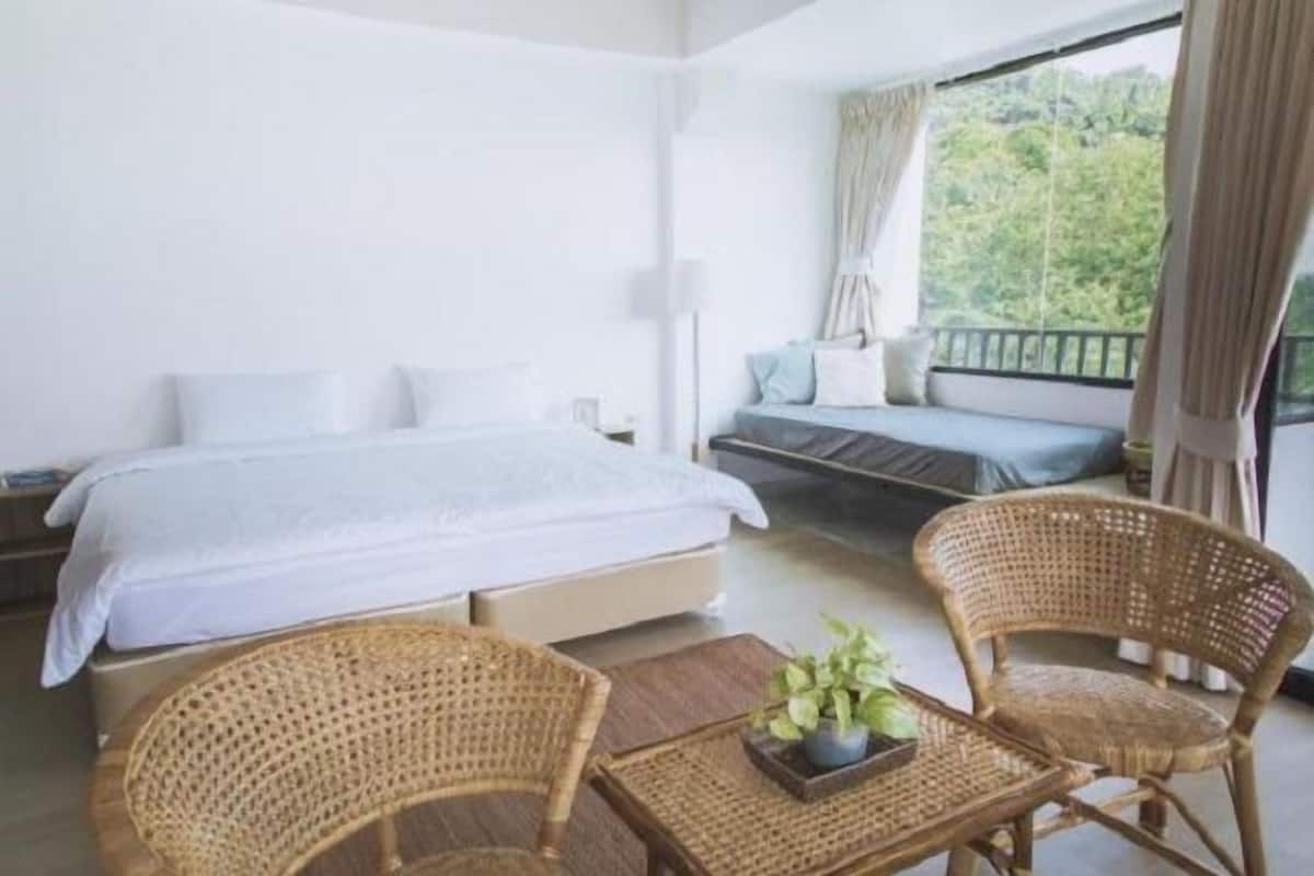 Ein Schlafzimmer mit einem Bett, einem Schlafsofa, zwei Korbstühlen und einem Tisch mit einer Pflanze.
