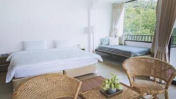 Een slaapkamer met een bed, een slaapbank, twee rieten stoelen en een klein tafeltje met een plant.