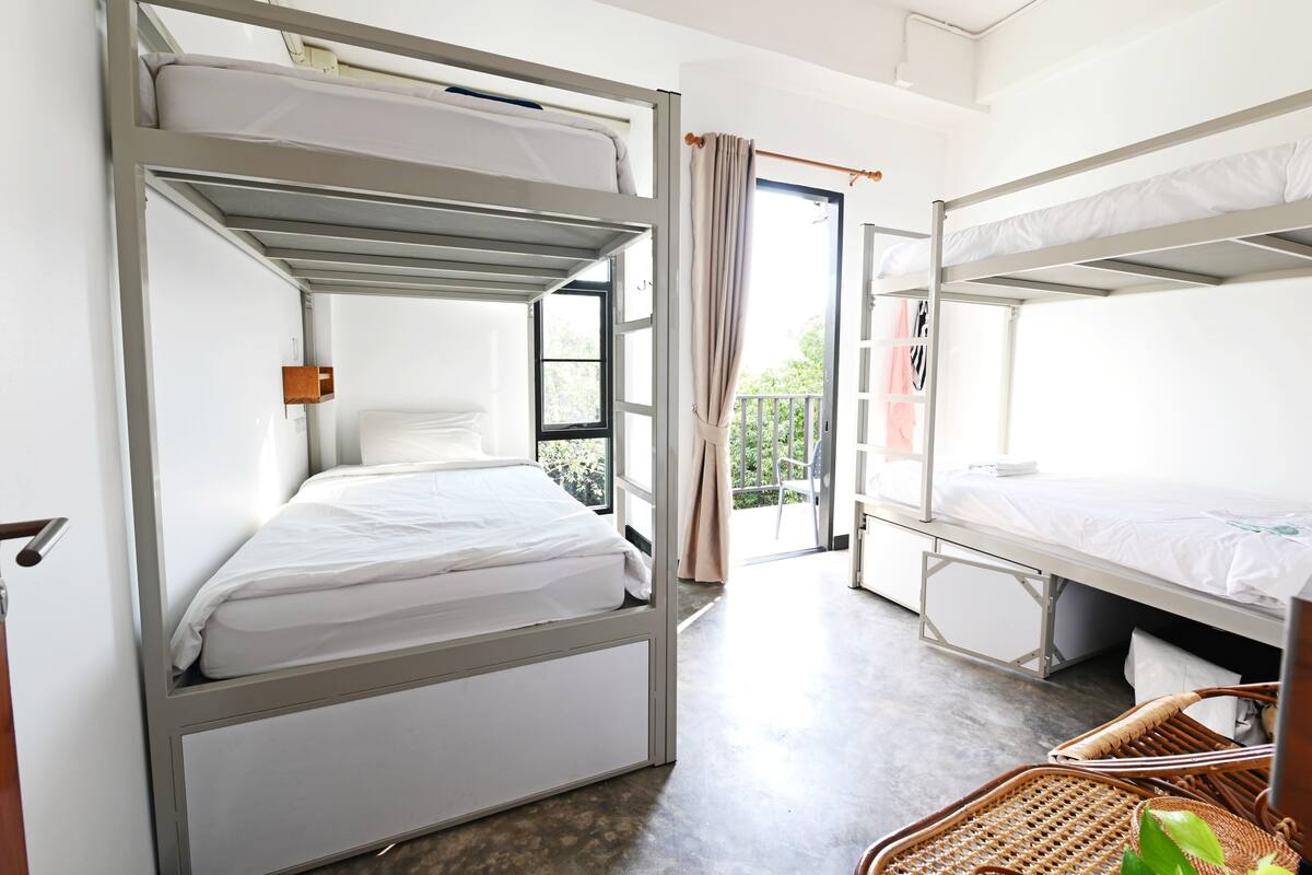 Ein Zimmer mit Etagenbetten, einem Fenster mit Vorhängen und einem Korbsessel.