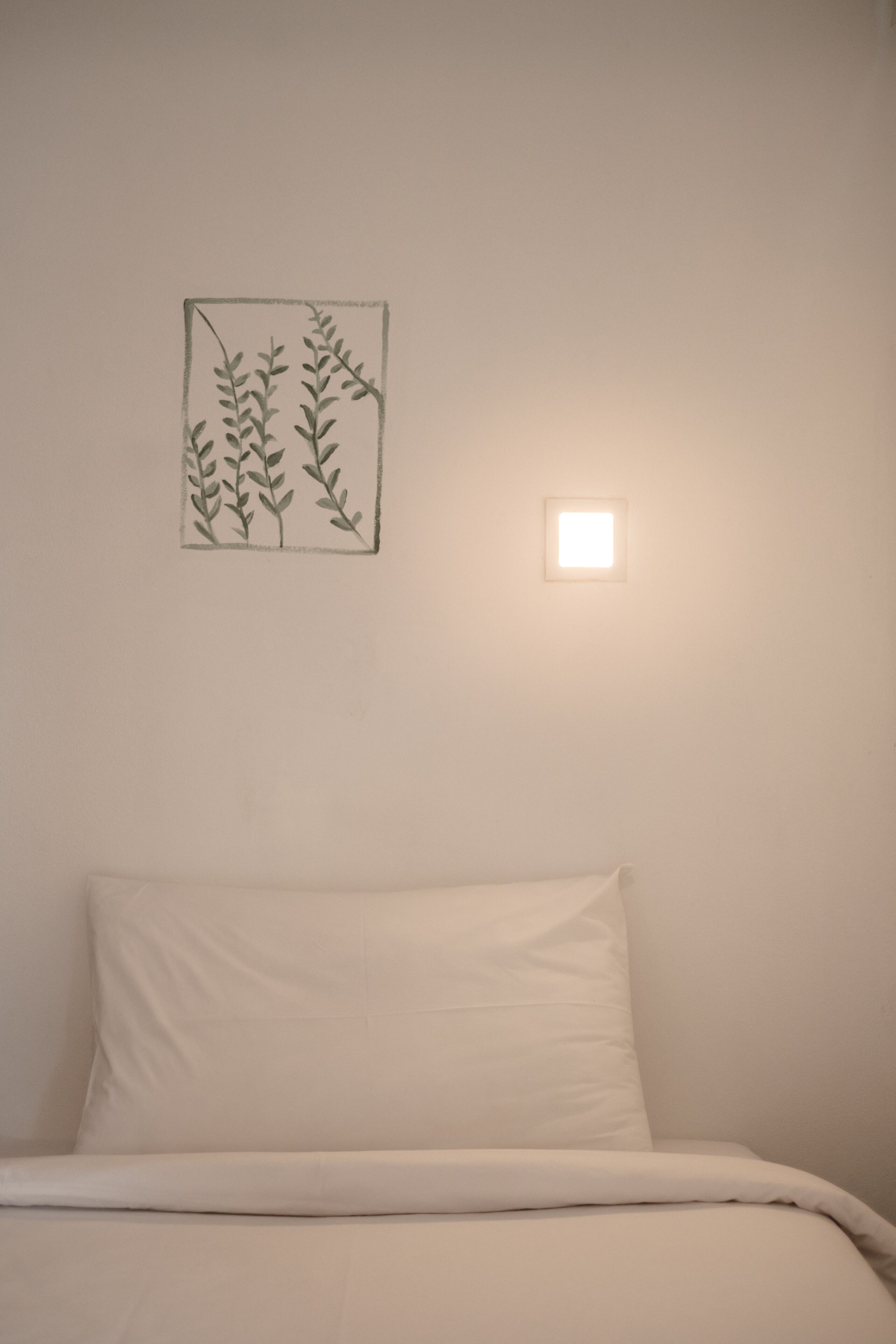 Un dormitorio con una cama, una lámpara de pared y un dibujo de una planta enmarco.