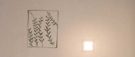 Un dormitorio con una cama, una lámpara de pared y un dibujo de una planta enmarco.