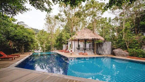 Une terrasse en bois entoure une piscine à l’eau d’un bleu cristallin, agrémentée de chaises longues et d’une structure à toit de chaume.