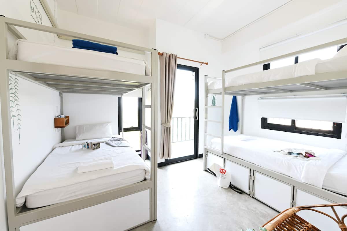 Ein Hotelzimmer mit Etagenbetten, einem kleinen Tisch mit Lampe und Blick auf den Balkon.