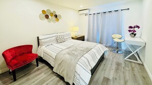 Un dormitorio con una cama, una silla roja, un escritorio con una planta y una obra de arte en la pared.