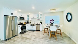 Una cocina moderna con armarios blancos, electrodomésticos de acero inoxidable y un comedor con mesa y sillas redondas.