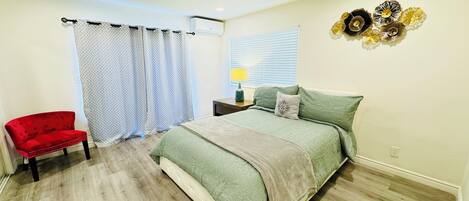 A bedroom with a bed, a red chair, a window with blinds, and decorative wall art.