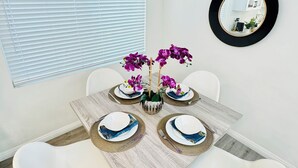 Un comedor con una mesa redonda, sillas blancas y orquídeas púrpuras.