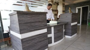 A reception desk with a marble finish, a man standing behind it, and a statue on top. - HOTEL DHARAMSHALA PARADISE (Dharamshala)