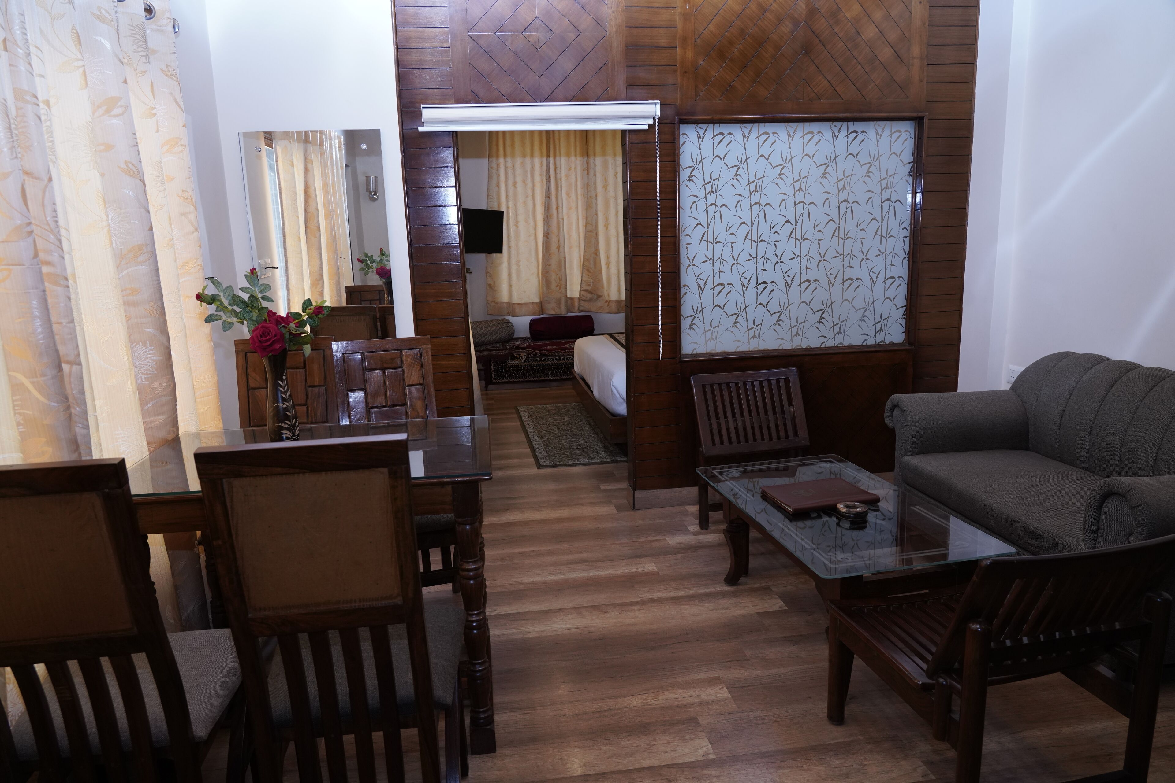 A modern living room with a sofa, a glass coffee table, wooden chairs, a dining table, and a TV.