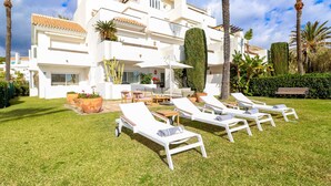 Een moderne witte villa met een ruim terras, buitenmeubels en een verzorgd gazon.