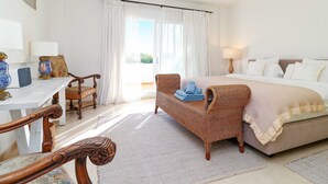 Een slaapkamer met een bed, een rieten stoel, een bureau en een raam met gordijnen.