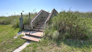 Una escalera de madera que sube hacia un edificio, rodeada de césped y plantas.