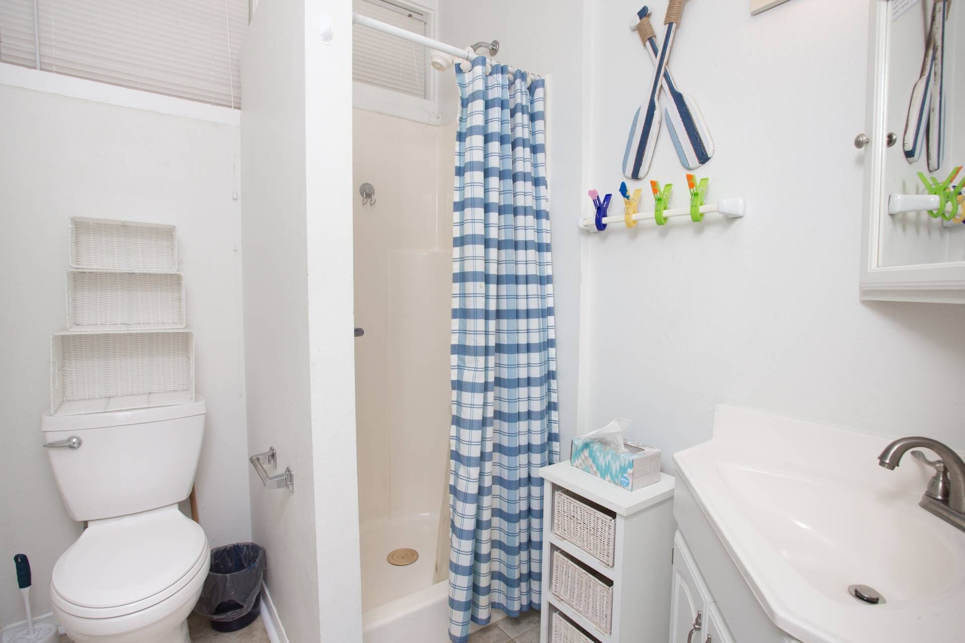 A bathroom with a white toilet, a shower with a blue and white checkered curtain, a sink with a mirror, and toiletries on a shelf.