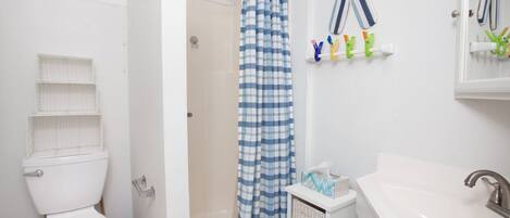 A bathroom with a white toilet, a shower with a blue and white checkered curtain, a sink with a mirror, and toiletries on a shelf.