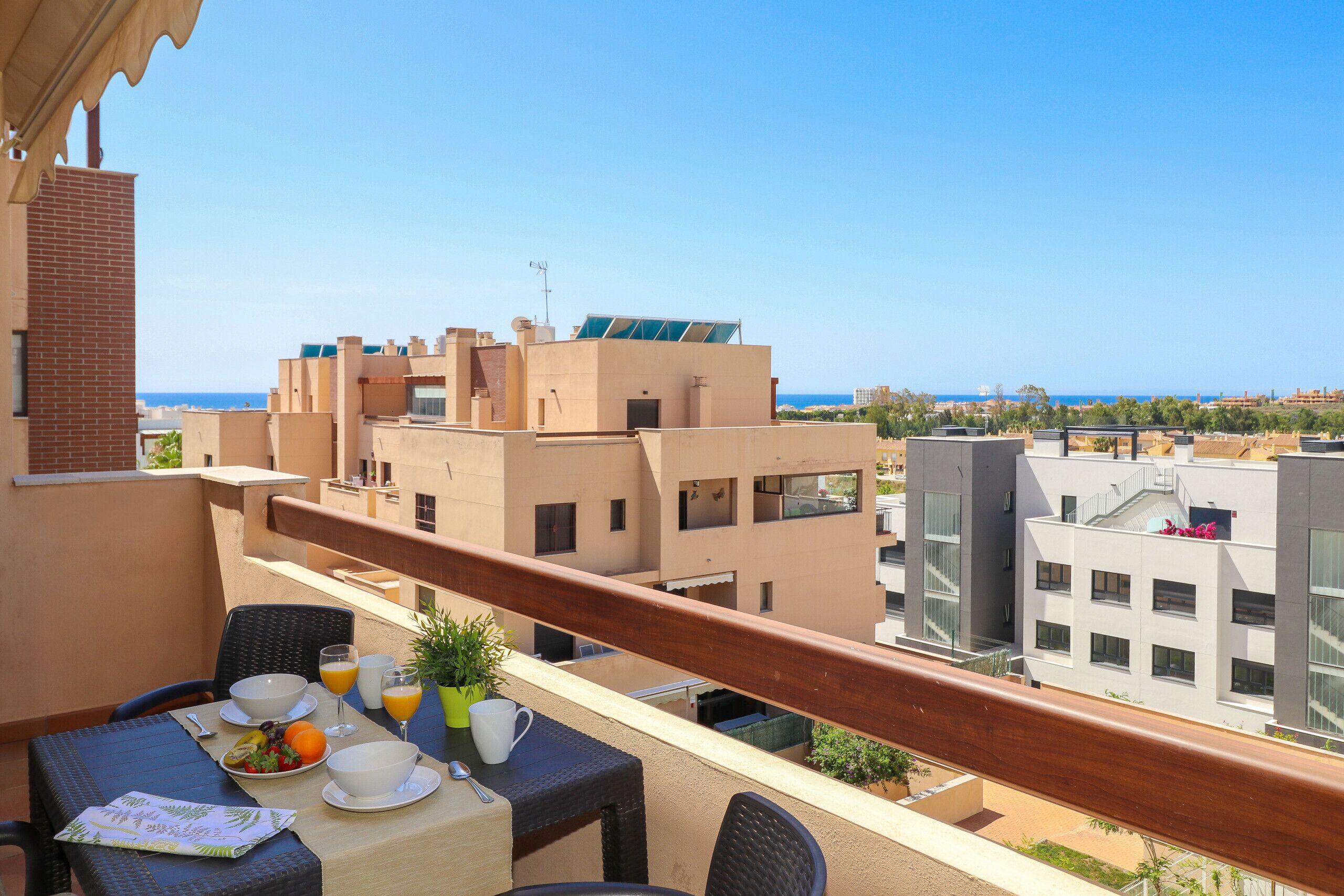 Ein Balkon mit einem für das Frühstück gedeckten Tisch, mit Blick auf eine Skyline und das Meer.