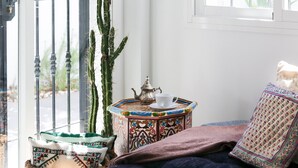 A cozy room with a cactus, a small table with a teapot and cup, and a cushioned chair.