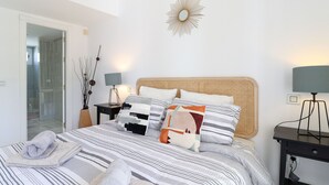 A neatly arranged bedroom with a bed, pillows, a bedside table, a lamp, and a wall-mounted mirror.