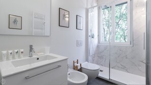 A modern bathroom with a large white sink, a toilet, and a shower area. There are framed pictures on the wall and a window providing natural light. - Italianway Easy - Caterina da Forl 6 (Milan)
