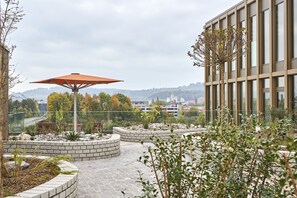 Un jardín en la azotea con espacios de estar, un paraguas grande y vistas de un paisaje urbano.