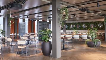 A spacious indoor area with multiple tables and chairs, large potted plants, and a modern ceiling design with exposed beams and lighting fixtures.