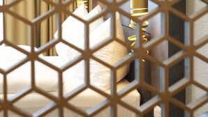 A hotel room with a geometric patterned partition, a bed with pillows, and a lamp. - Lumen Apartments (Schenkon)