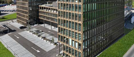 Ein modernes Gebäude mit der Aufschrift "Lumen Park" auf dem Dach. Es verfügt über einen Parkplatz mit Pfeilmarkierungen und eine grüne Rasenfläche.