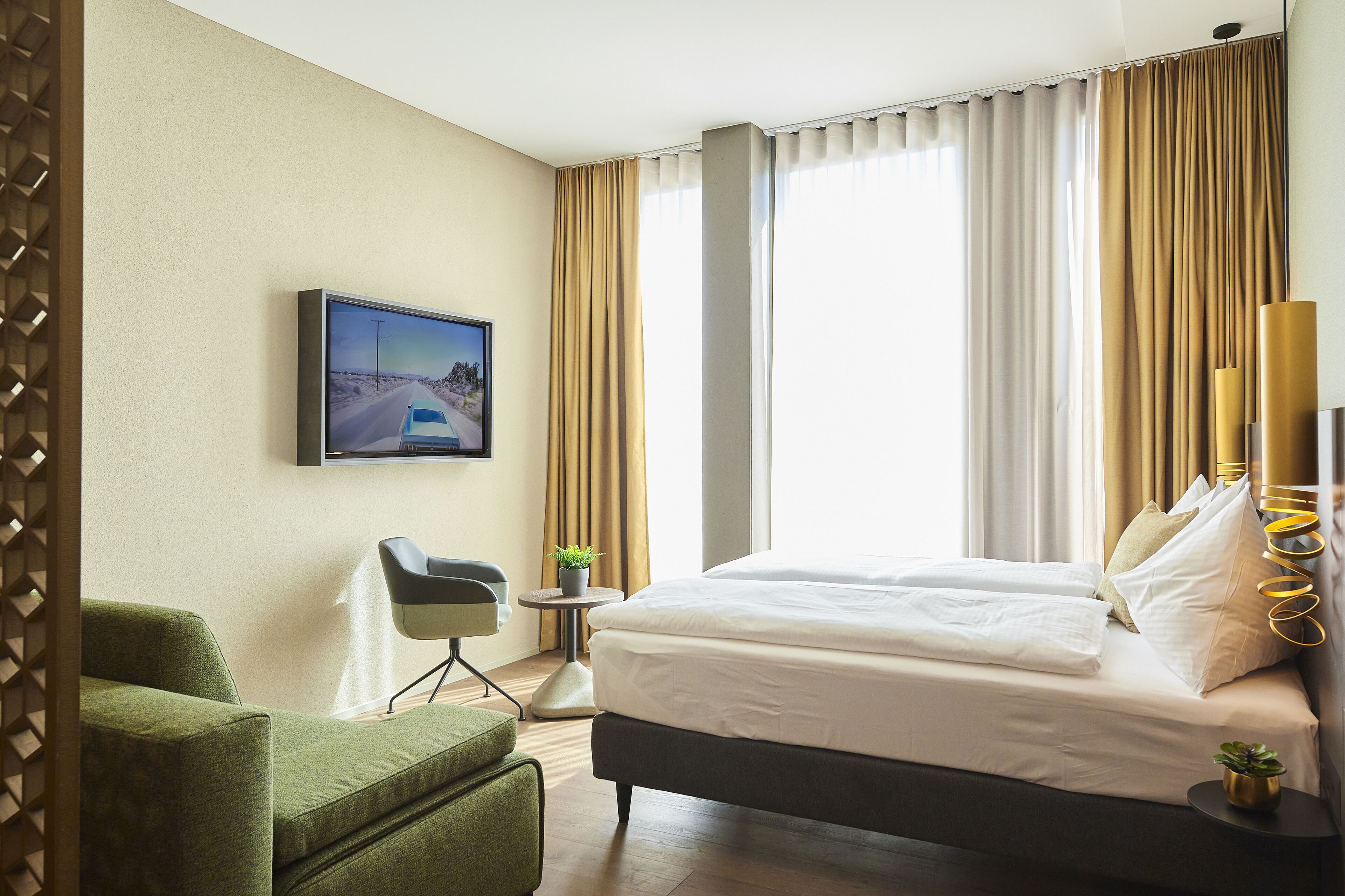 Una habitación de hotel con una cama, una silla, una mesita con una planta y un televisor en la pared.