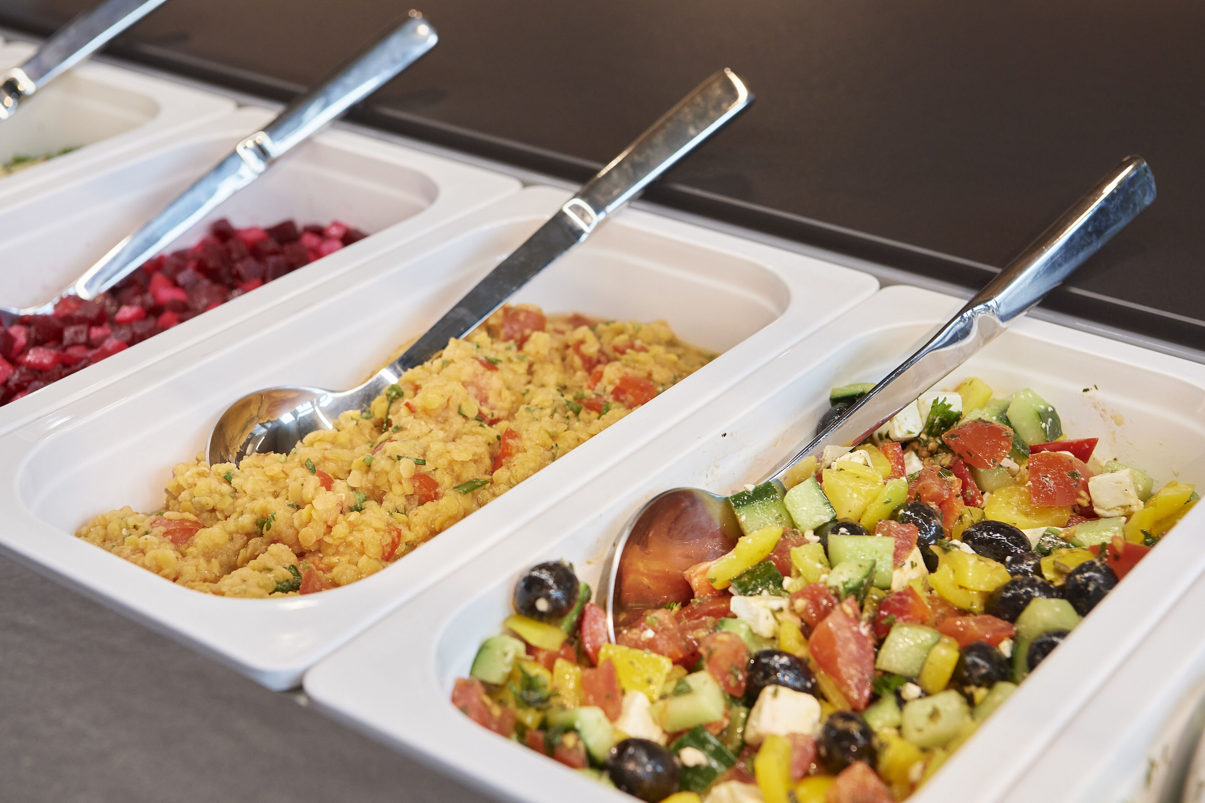 Three food dispensers with spoons, containing different dishes.
